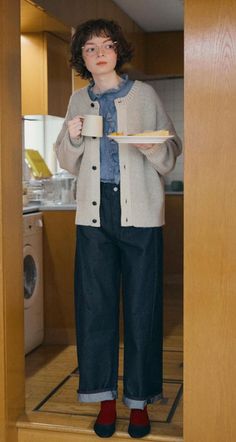 Person with short curly hair and glasses holding a mug and plate in a kitchen