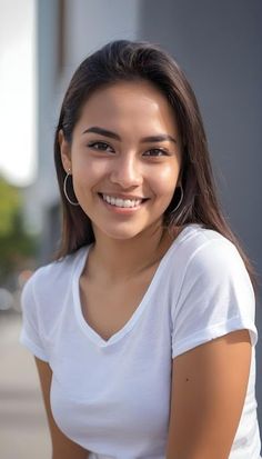 Young woman with long dark hair smiling in a white t-shirt outdoors