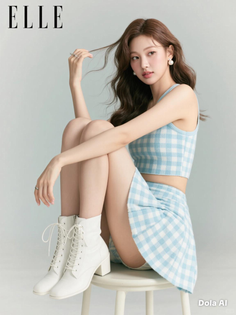 Woman with long wavy hair in a blue plaid top and skirt, sitting on a stool