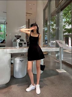 Woman in a black dress and baseball cap covering her face indoors