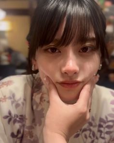 Woman with black hair and bangs wearing a floral print top, holding her chin