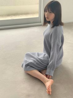 Woman in a light blue ribbed dress sitting on the floor indoors