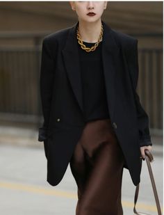 Woman in a black blazer and brown skirt with a gold necklace