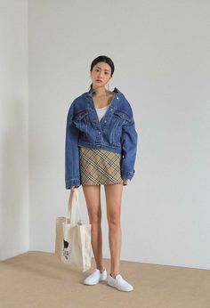 Woman in a denim jacket and plaid skirt holding a tote bag indoors