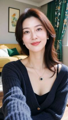 Woman with long hair wearing a dark cardigan and necklace indoors