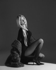 Woman with blonde hair in a black bodysuit and fur coat in a dramatic pose
