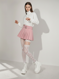 Woman in a pink pleated skirt, white jacket, and patterned tights in a studio