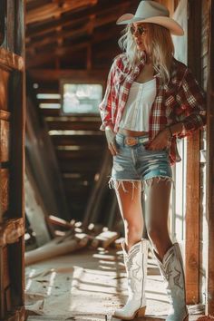 Woman in a cowboy hat, plaid shirt, and denim shorts standing indoors