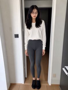 Woman with long black hair and glasses wearing a white shirt and grey leggings
