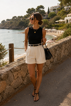 Woman in white shorts and a black top walking along a stone wall overlooking a beach