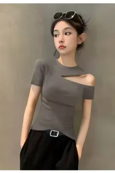Woman in a gray top with an exposed shoulder and black pants indoors