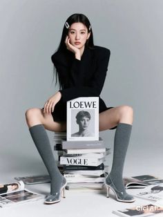 Woman in a black blazer and knee-high socks sitting on a stack of magazines