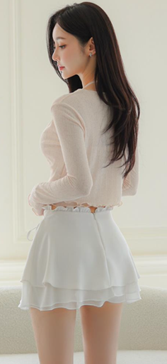 Woman with long dark hair wearing a light top and white ruffled skirt indoors