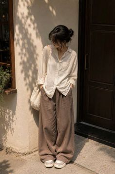 Woman in a loose shirt and wide leg pants standing outdoors with soft lighting