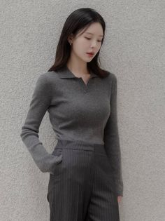 Woman with long dark hair wearing a gray top and pinstripe pants indoors