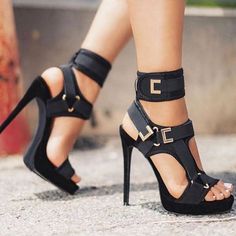 Close up of a person wearing black high heels with gold buckles