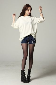 Woman with long hair wearing a white top, denim shorts, black tights, and combat boots