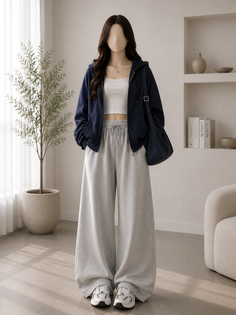 Woman in a navy hoodie, white crop top, and grey sweatpants indoors