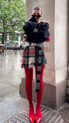 Woman in a plaid skirt, red tights, and black top posing outdoors