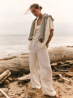 Woman in linen pants and a striped sweater on a beach with driftwood