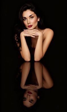 Woman with dark hair and red lipstick posing against a dark background with reflection