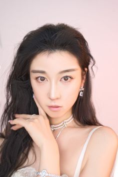 Woman with long dark hair and jewelry against a pink background