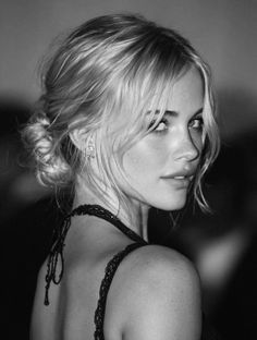 Woman with blonde hair in an updo wearing a lace top, looking over her shoulder