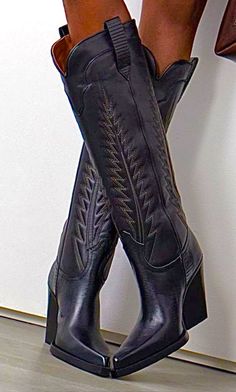 Person wearing black cowboy boots with embroidered design and high heels