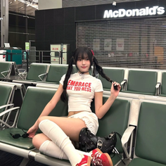 Woman with pigtails in a white crop top and shorts sitting in an airport