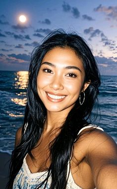 Woman with long dark hair smiling at the beach at night with a full moon
