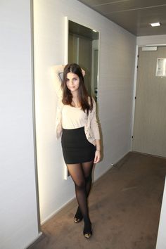 Woman in a black skirt and tights posing in an indoor hallway