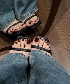 Feet in black sandals with painted toenails and denim jeans on a wooden floor