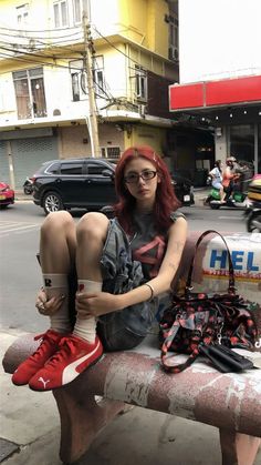 Person with red hair and glasses sitting on a bench on a street