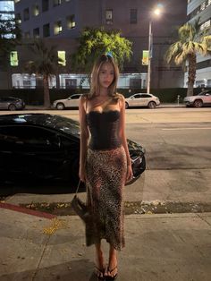 Woman in a black corset top and leopard print skirt on a city street at night