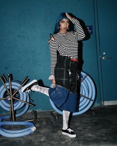 Woman with blue hair in a striped shirt and plaid skirt posing indoors
