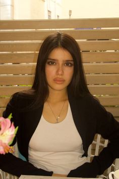 Woman with long dark hair wearing a white tank top and black jacket indoors