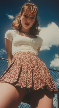 Woman in a floral pleated skirt and white top from a low angle against a blue sky