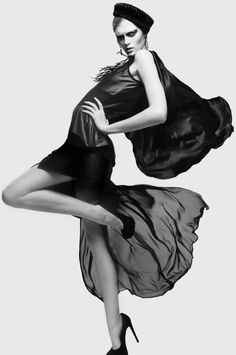 Woman in a black dress and hat posing dramatically in a studio