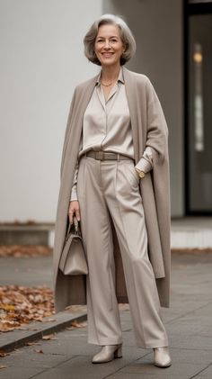 Woman with gray hair in a long cardigan and wide leg pants holding a handbag
