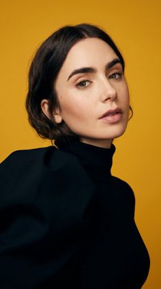 Woman with dark short hair and a black turtleneck against a yellow background