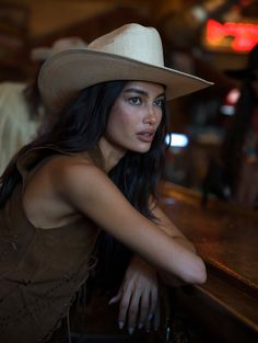 Woman in a cowboy hat and brown vest leaning on a bar counter