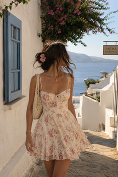 Woman in a floral dress walking down a street in Mykonos with ocean view
