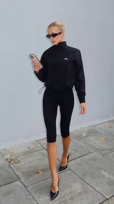 Woman in black activewear and high heels walking outdoors while looking at her phone