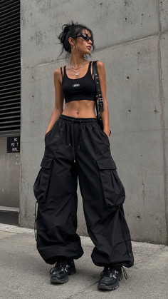 Woman in a black crop top and baggy cargo pants posing against a concrete wall