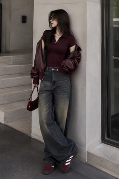 Woman in a maroon polo shirt and wide leg jeans leaning against a wall