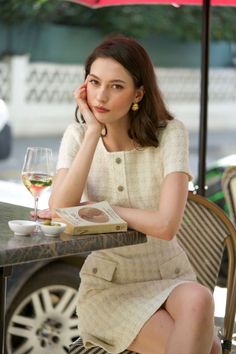 Woman in a tweed dress sitting at an outdoor cafe with a book and wine