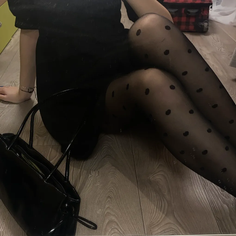 Person in a black dress and polka dot tights sitting on a wooden floor