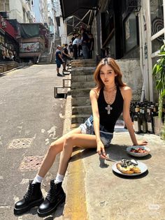 Woman in denim shorts and a black top sitting on a street with food
