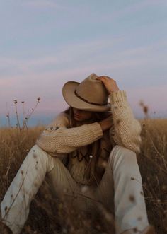 Person in a cowboy hat and knitted sweater sitting in a field at dusk