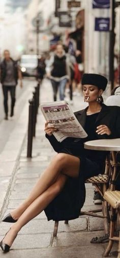 Woman in a black dress and hat reading a newspaper at an outdoor cafe
